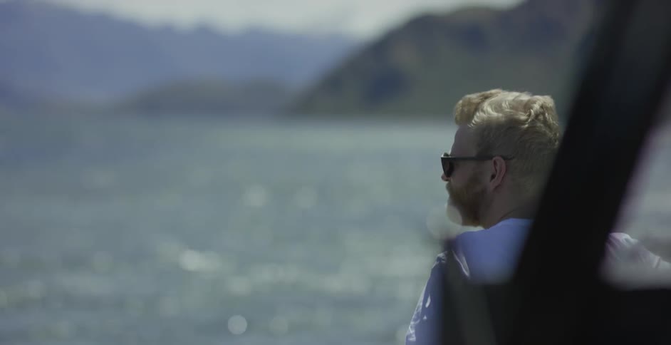 Man wearing sunglasses looking out to the waters from the shore