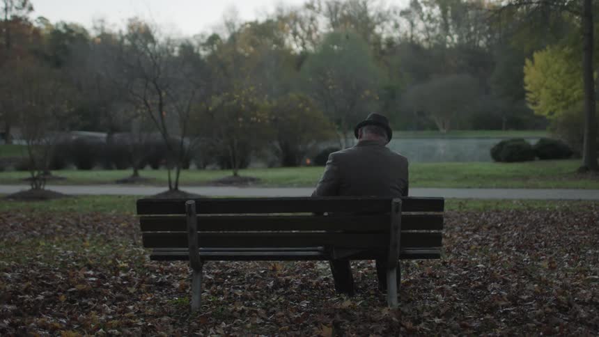 A man sits on a park bench in the fall