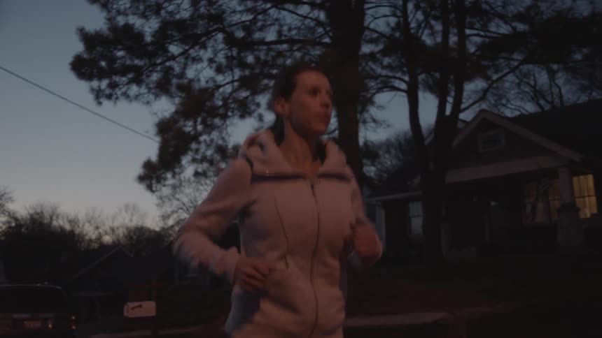 A woman jogs on a residential street at dusk