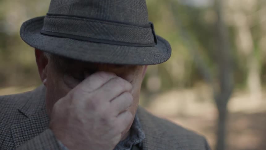 A man in a hat takes off his sunglasses and rubs his nose
