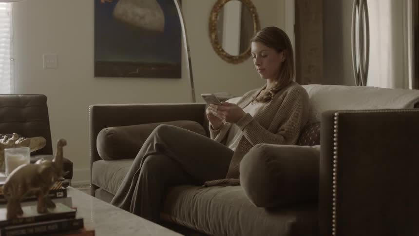 A woman sitting on a living room couch is using her cell phone