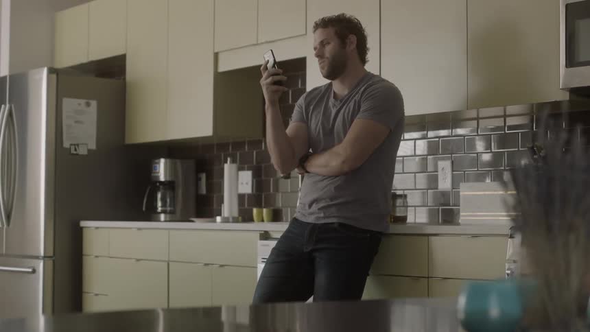 A man standing in a kitchen is checking his cell phone