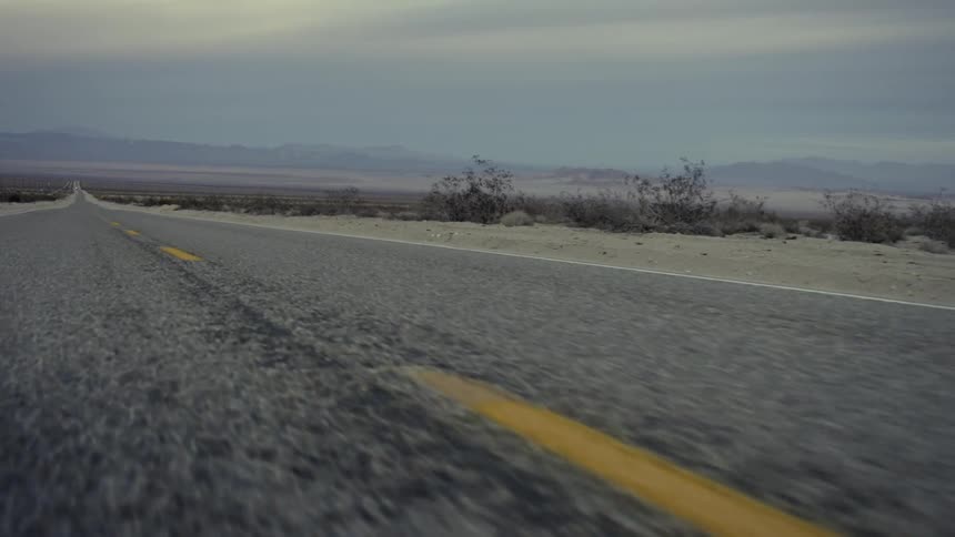 Moving view of a barren road headed towards some mountains on a cloudy day