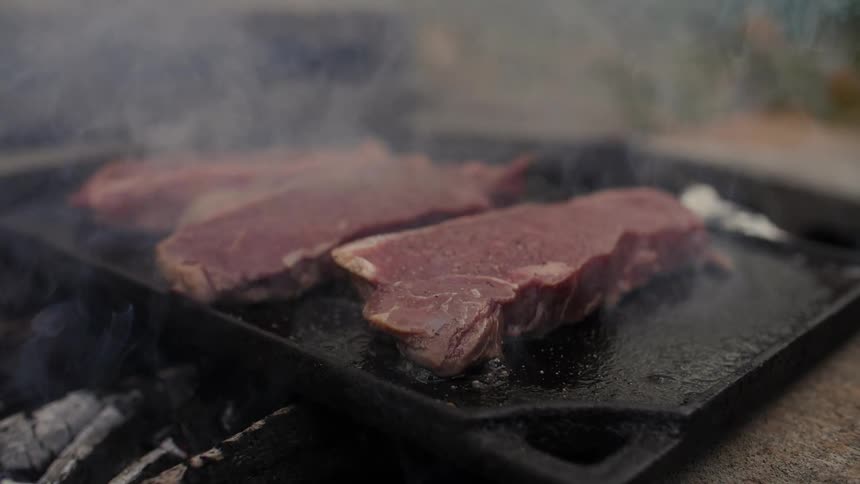 Steaks cook over a smoky fire