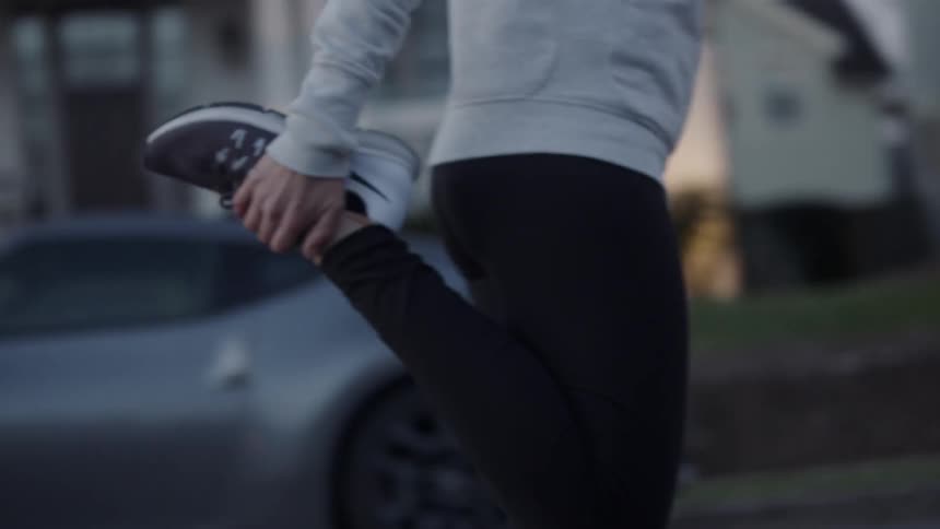 A woman stand outside in a residential area stretching her leg muscles