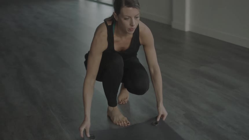 A woman unrolls a yoga mat on a studio floor