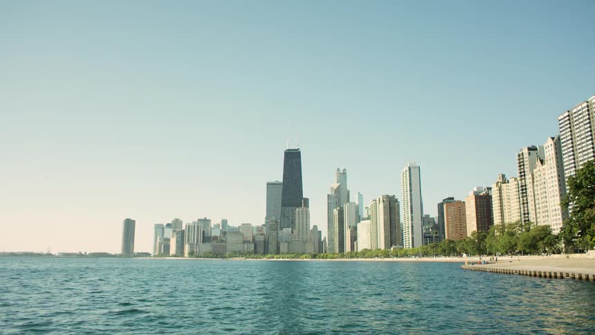 The sun shines on the water and tall buildings of an ocean side city