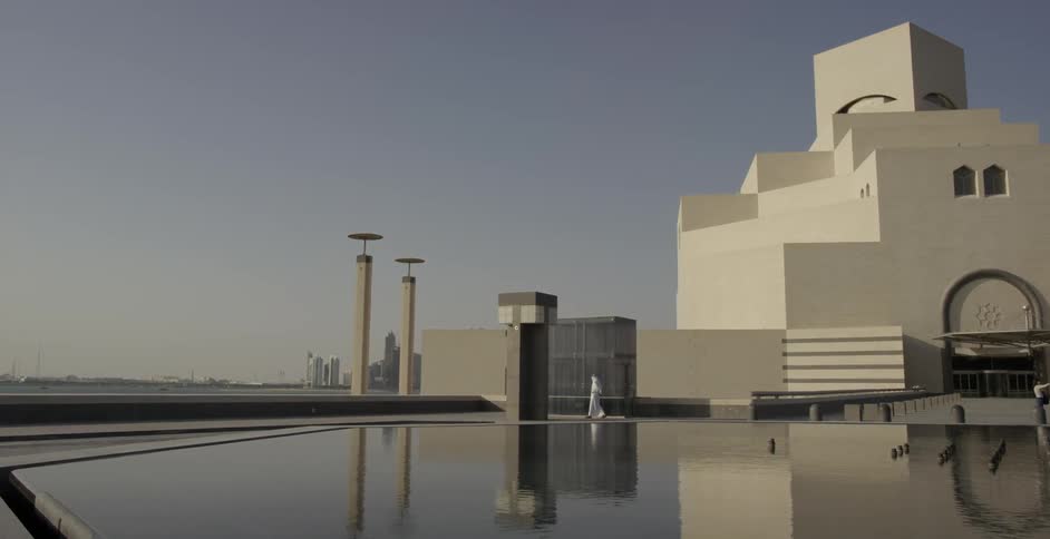 A person walks near a white building and water feature