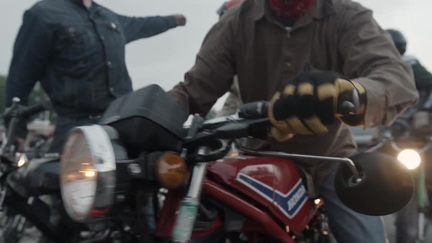 A group of people riding motorcycles at dusk is stopped and talking