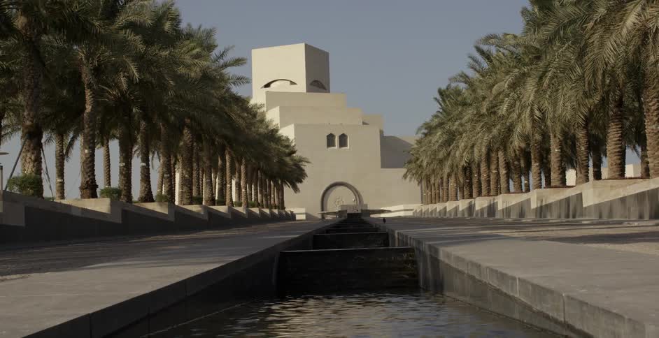 A water feature flows in front of a white building and palm trees