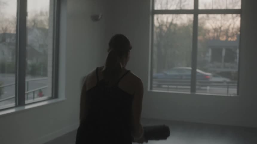 A woman unrolls a yoga mat on a studio floor