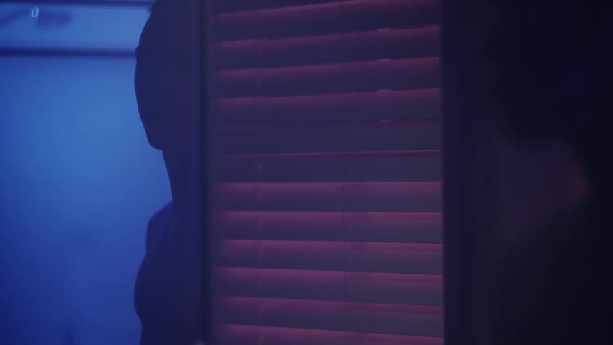 A man stands near blinds in a dark room