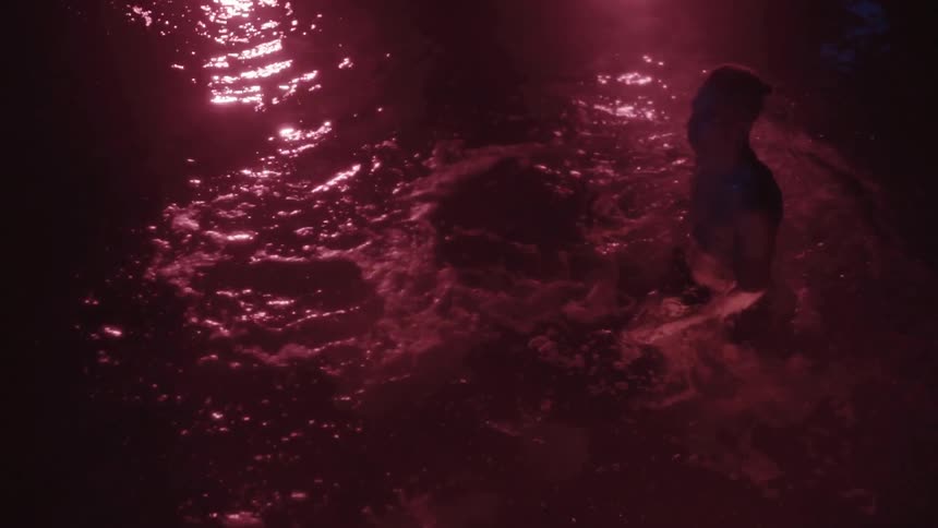 Person swims in water lit with a purple hue