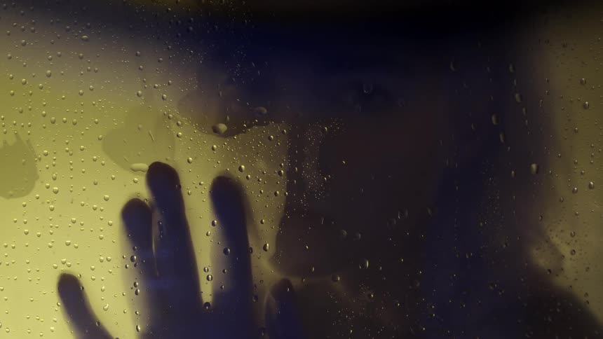 Person on the other side of a piece of wet glass rubs their hand down it