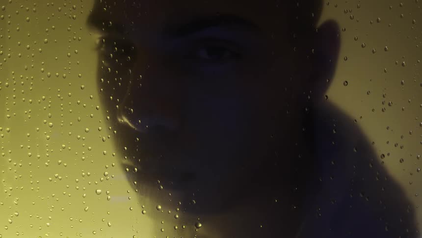 Man looking through a glass with water dots on it