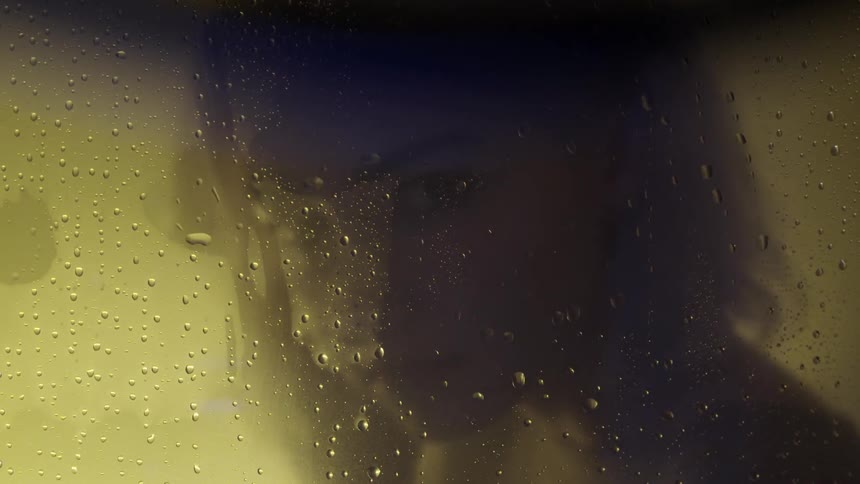 A woman looks through steamy glass while showering