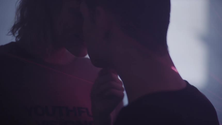 A woman holds a man's chin and neck as they kiss