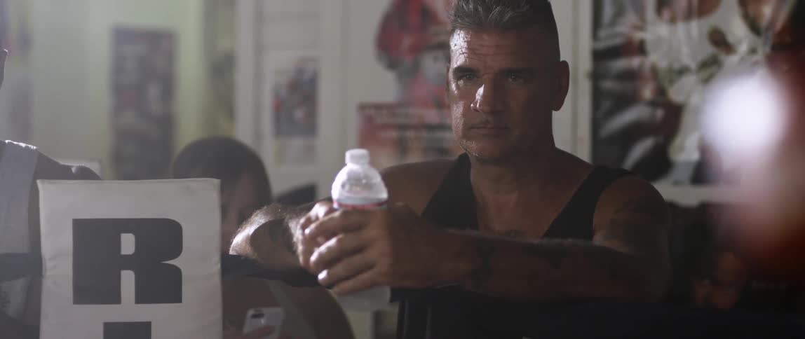 A man holding a bottle of water watches boxers in the ring