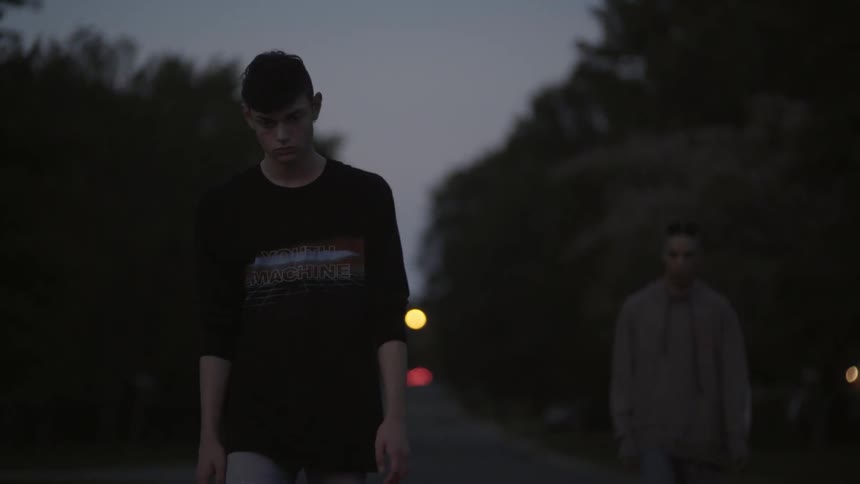 Two teenage boys are walking down a road at dusk