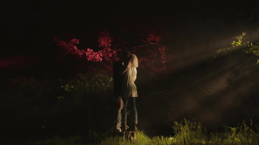 Two people kissing in a field with trees