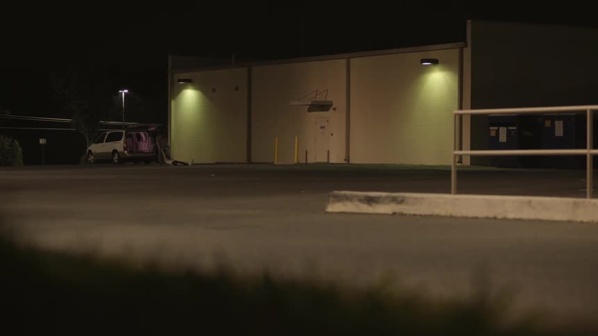 Man dragging a body to a trunk in a parking lot