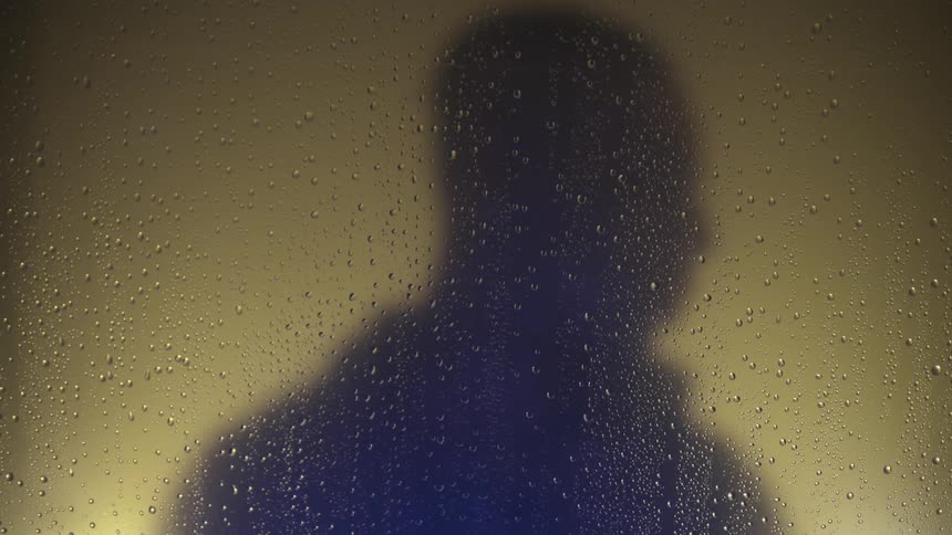 A man turns his head near a water spotted window