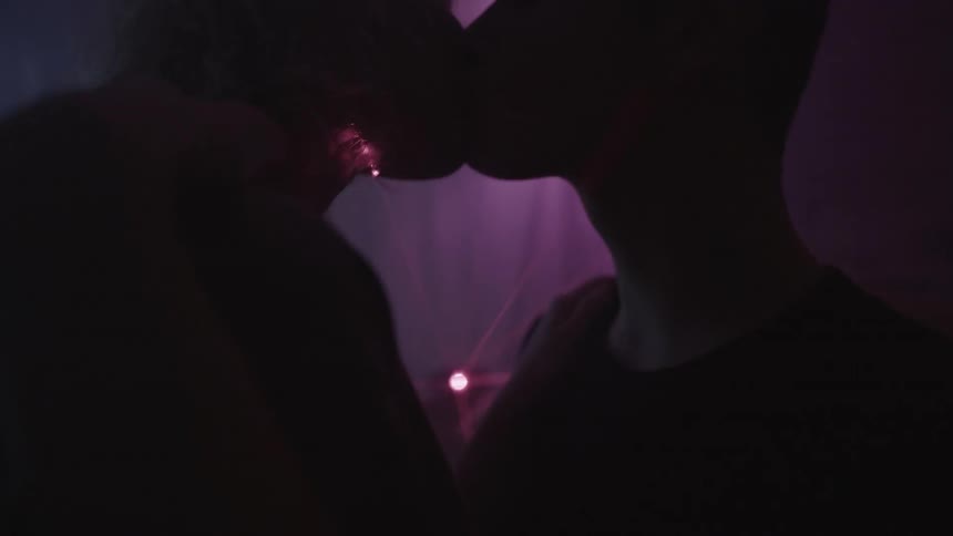 A couple kiss in a room lit by laser lights