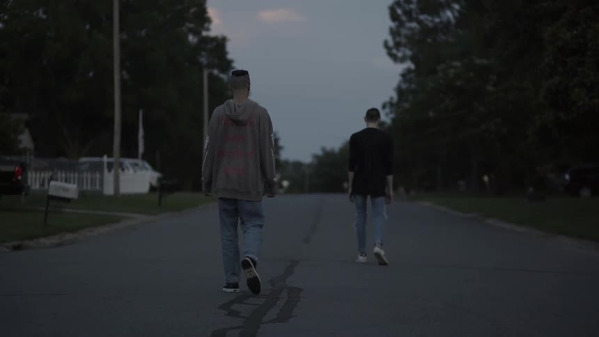 Two young men walk down a street near dusk