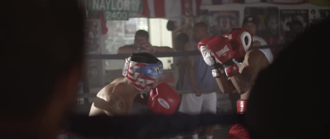 A group of people are standing around a boxing ring watching two people box