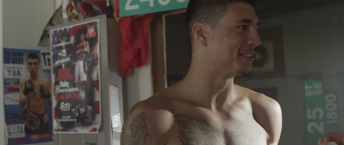 Tattooed man wearing boxing gloves drinking from a water bottle in a gym