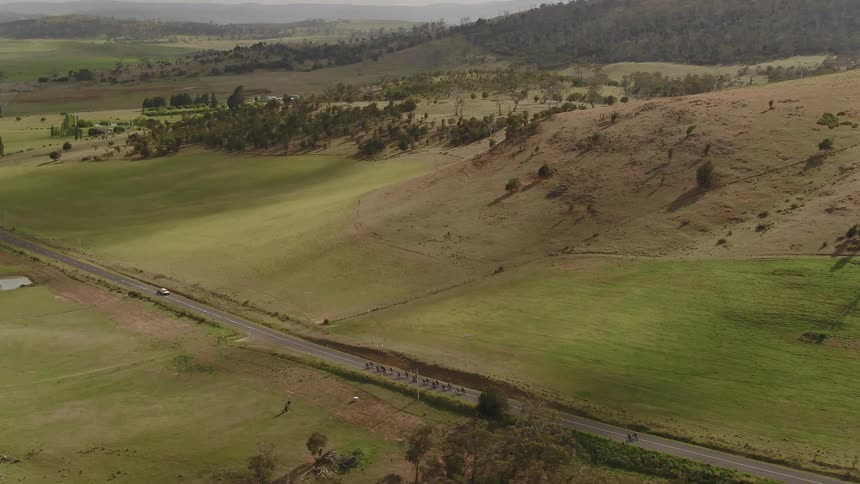 A line of people on bicycles travels down a country road