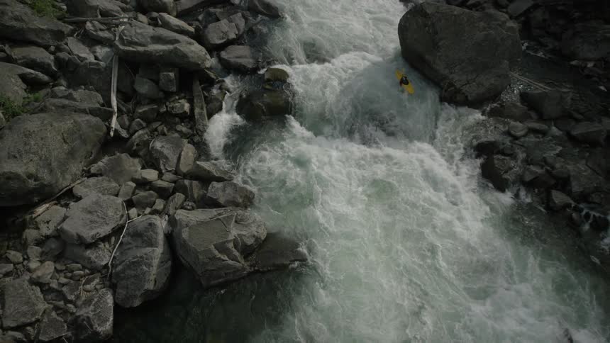 A person in a yellow kayak rides a rough river rapids