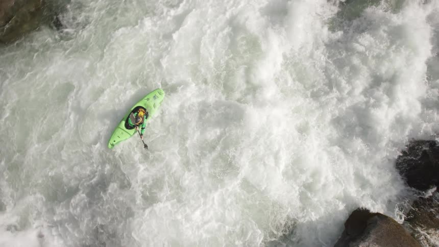 Person rafting down a river in a green kayak