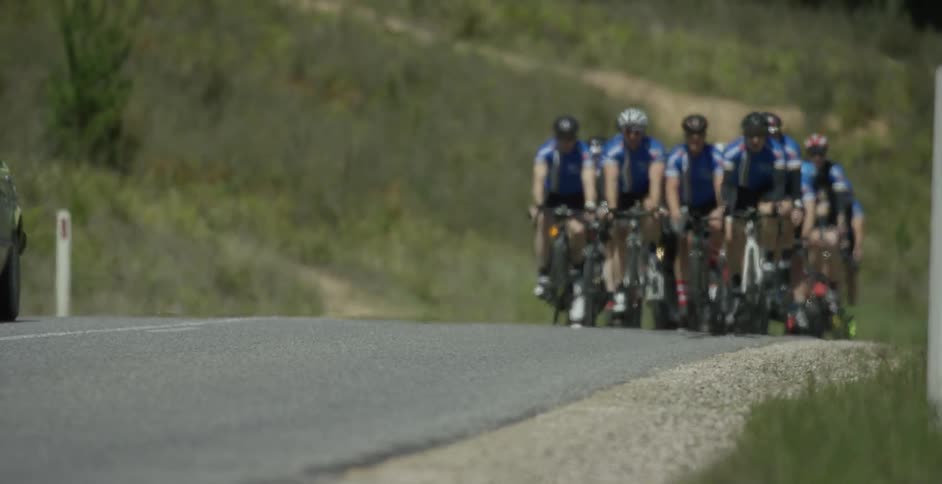 Green car travels ahead of a group of cyclists