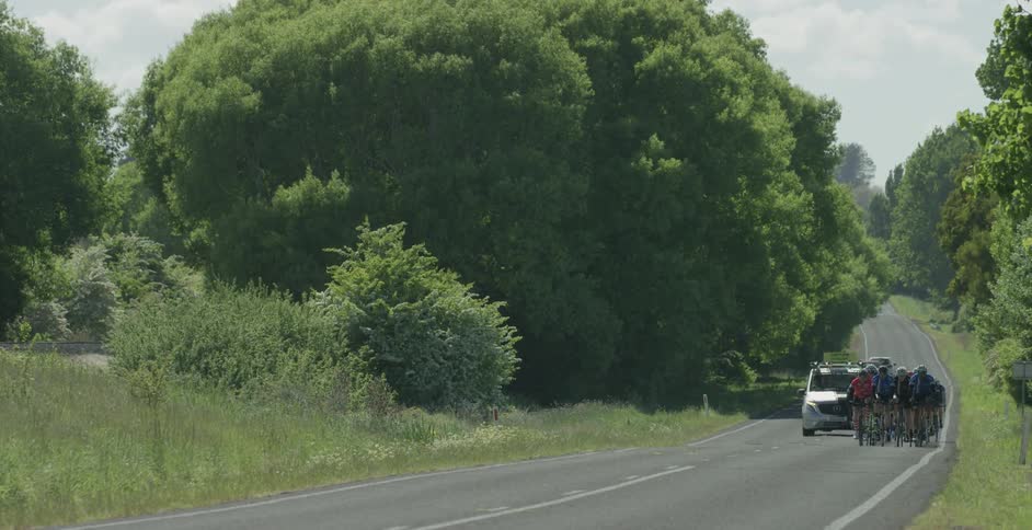 A group of bicyclists are escorted by a car as they ride down the road