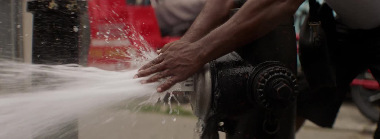 A man holds his hands in front of water shooting from a fire hydrant