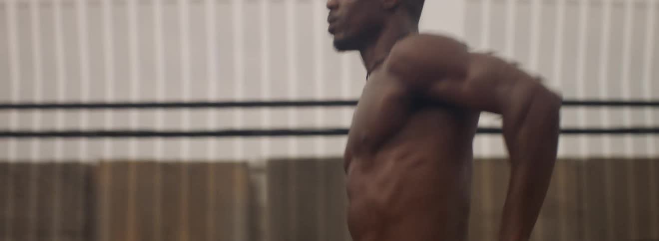 A shirtless man runs past a fence