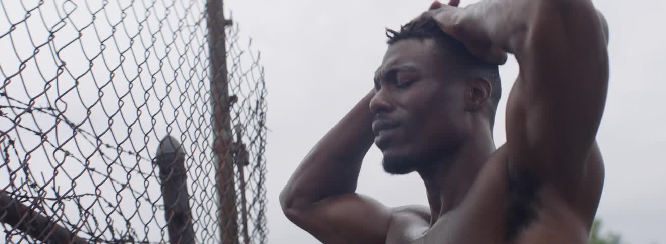 Shirtless man looks through a chain link fence