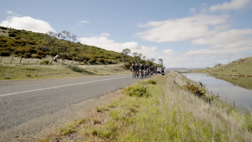 A white van follows a group of cyclists down the road