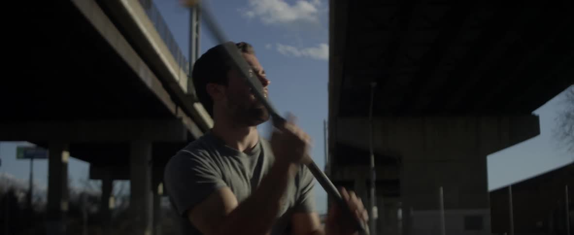 Man swings a lacrosse stick under a blue sky