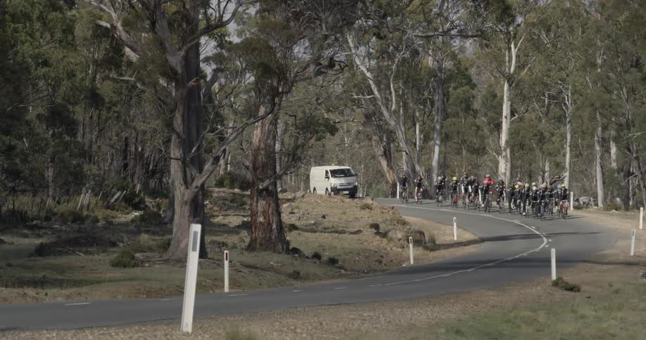 Large group of people riding bicycles with a van behind them