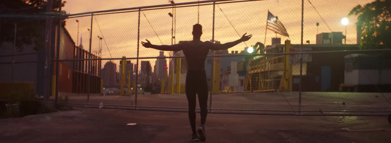 Man holding his arms out looking through a chainlink fence at sunset