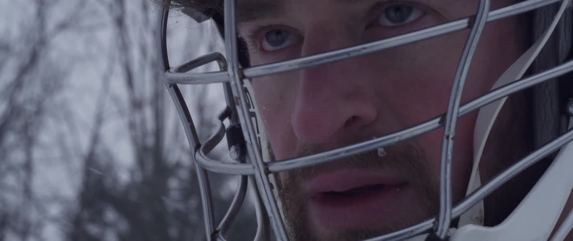 A man in a sports helmet stands outside while it snows