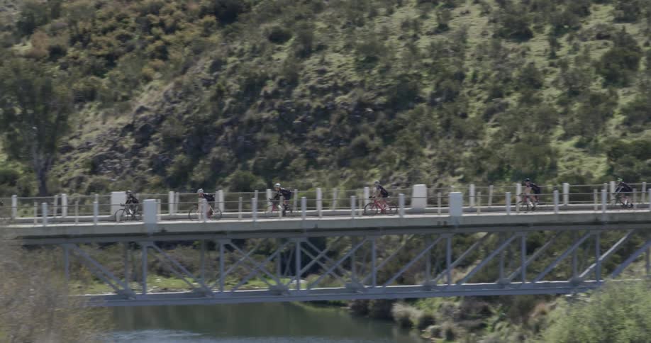 A long line of bicyclists travel across a bridge