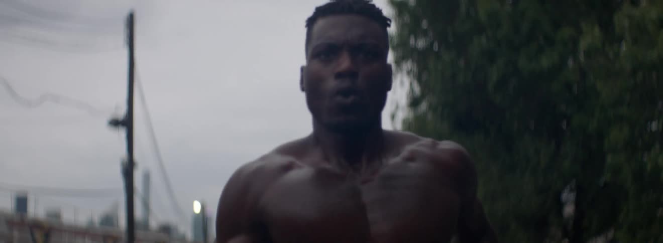Muscular man without a shirt jogs near some trees