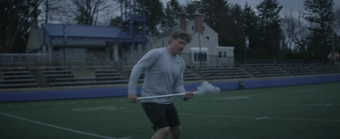A man scoops up a ball with a lacrosse stick and shoots