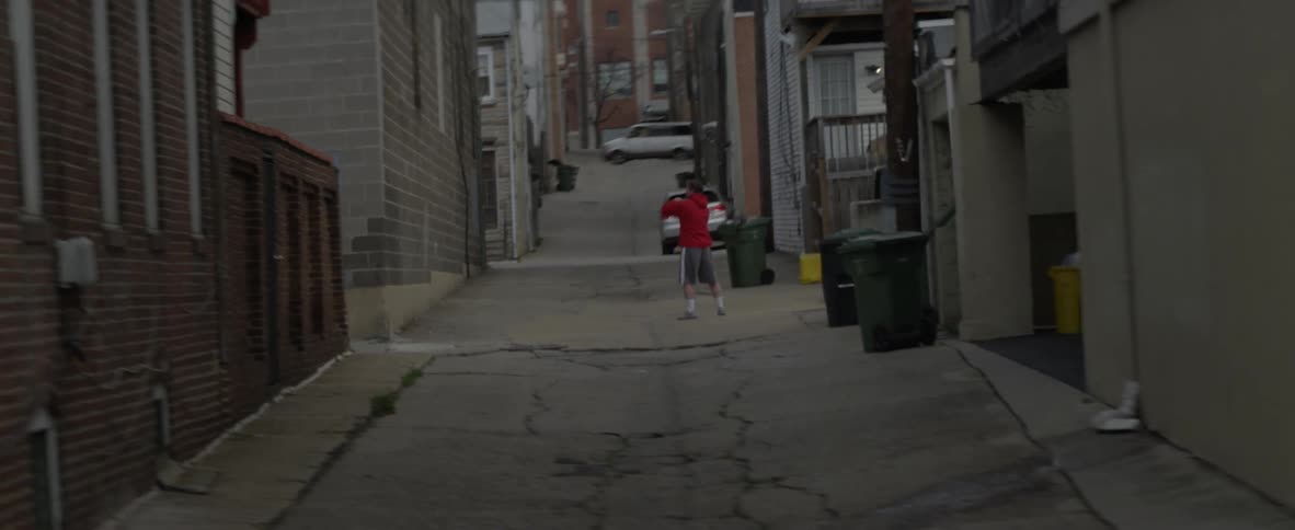A man bounces a ball off a building and catches it with a lacrosse stick