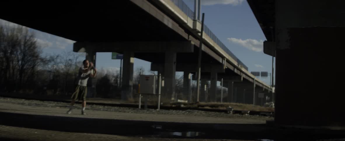 A man bounces a ball off a wall and catches it with a lacrosse stick