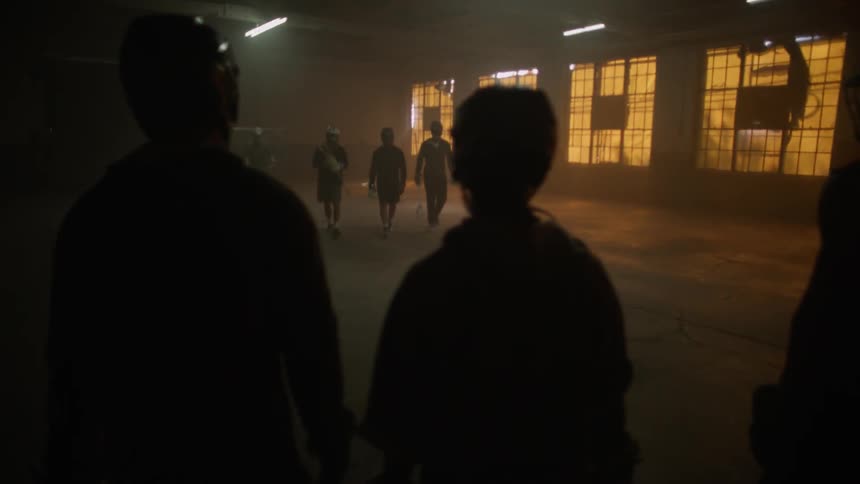 Group of people walk through a dim warehouse towards another group of people