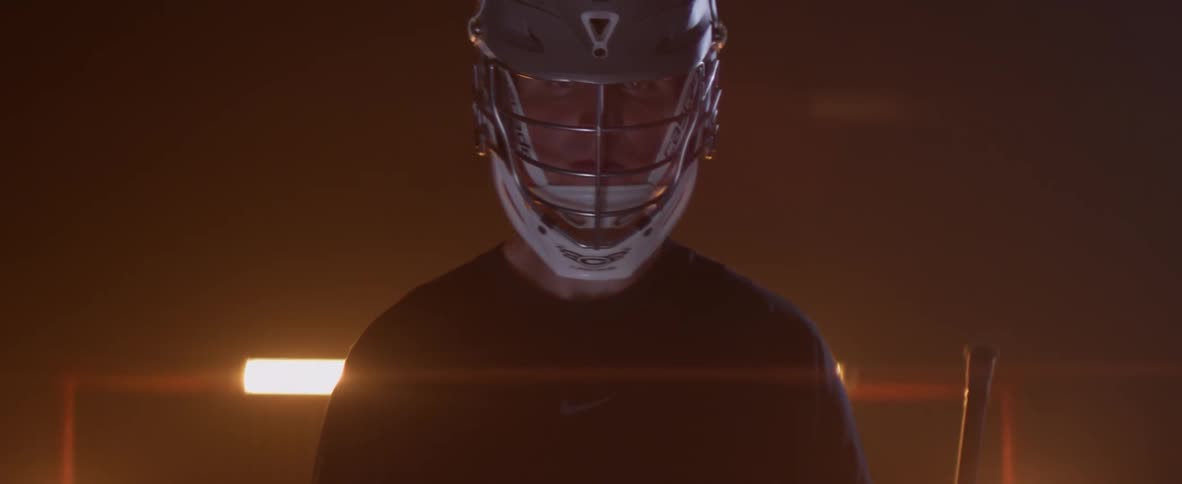 A lacrosse player stands in front of a glowing goal